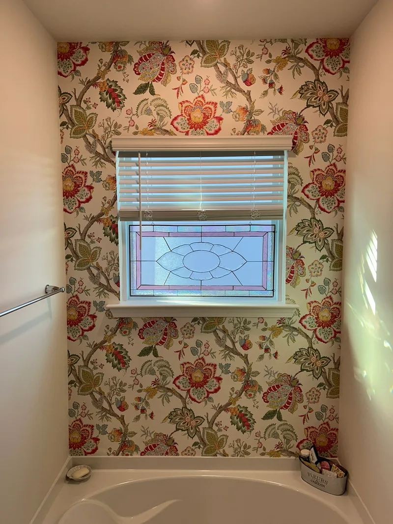 This charming bathroom features a vibrant chinoiserie-inspired floral wallpaper with twisting branches laden with oversized, multicolored blooms in rich reds, corals, pinks, and sunny yellows, accented by lush green leaves and subtle foliage details. Set against a soft cream or light neutral background, the intricate, repeating pattern evokes classic elegance with a fresh, lively twist—blending exotic botanical charm and timeless sophistication. Perfect as a bold accent wall, this design brings warmth, personality, and a touch of romantic flair to any space, making it an ideal choice for bathrooms, powder rooms, or cozy retreats seeking standout style. (Installed to stunning effect in a local Greer-area home!)