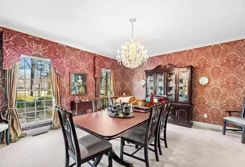 This elegant dining room is transformed by luxurious deep red damask wallpaper, featuring intricate, symmetrical floral and scroll motifs in rich crimson tones. The bold, classic pattern delivers depth, texture, and timeless sophistication, creating a warm, opulent backdrop with enduring historic charm. The wallpaper's detailed design and vibrant hue make a dramatic statement, instantly elevating the space into a refined, inviting retreat. Perfect showcase of how high-quality luxury damask wallpaper in rich red can redefine any room with dramatic elegance and style.