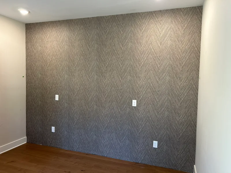 This striking office accent wall showcases a modern faux grasscloth wallpaper in a sophisticated chevron pattern. The textured, linear design in neutral gray tones creates depth and visual interest, transforming the space into a refined and contemporary workspace