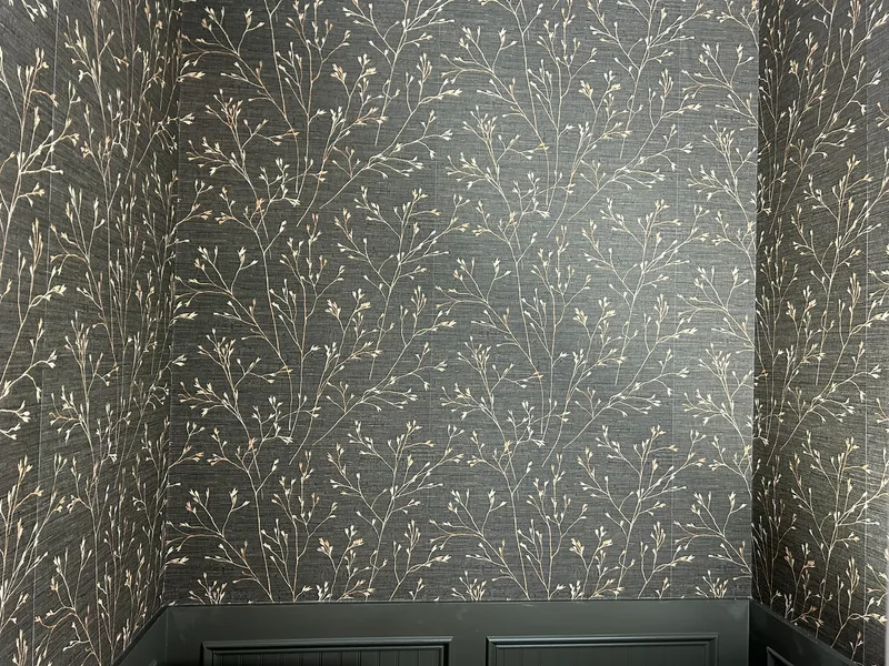 This sophisticated powder room features a luxurious printed faux grasscloth wallpaper with a delicate, branching botanical motif in metallic gold on a deep charcoal background. The elegant pattern adds subtle shimmer and texture, beautifully contrasting with the dark wainscoting below for a dramatic and refined look.